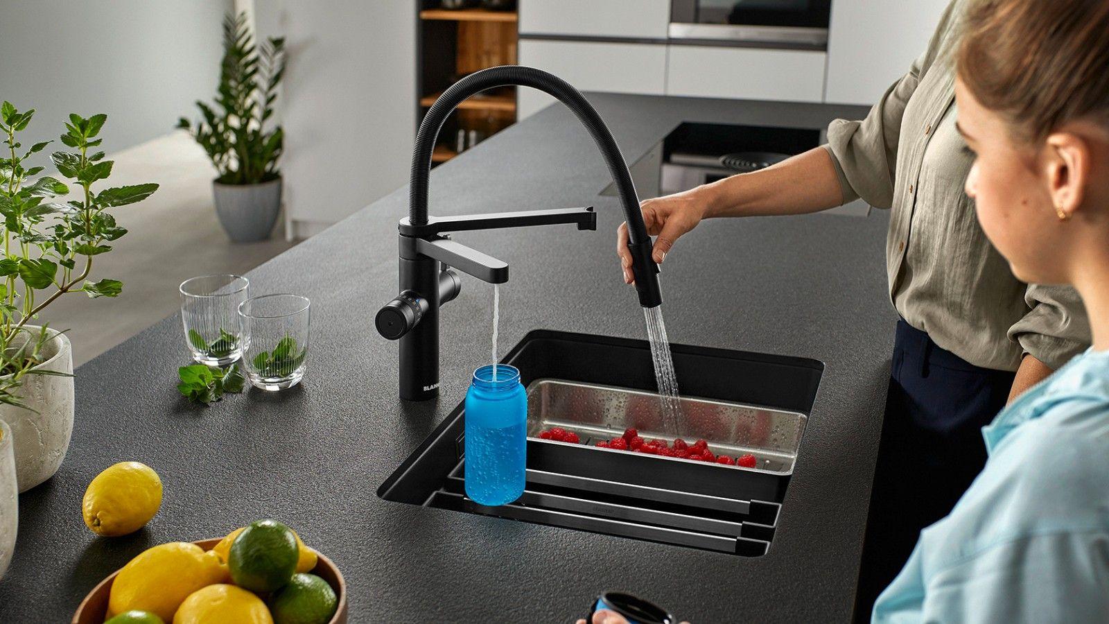 Hausgeräte — Schwarze Küche mit Armatur, zwei Frauen befüllen Wasserglas am Spülbecken